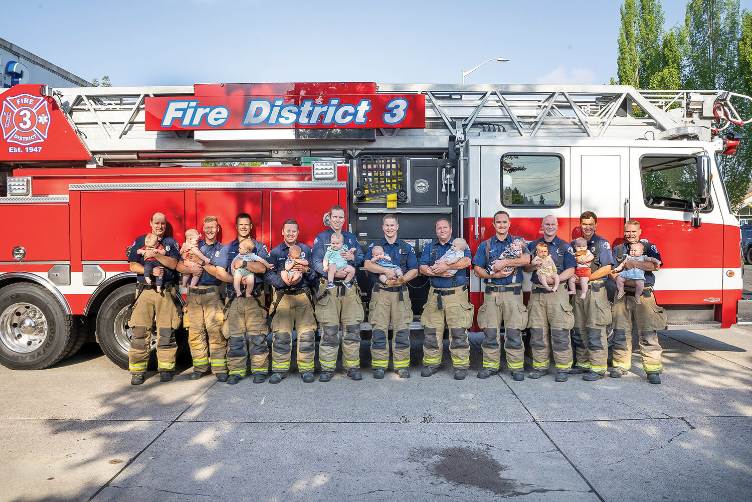 Thirteen Fire District No 3 firefighters stand with their babies who have been born since last November at Station 35 in Battle Ground.